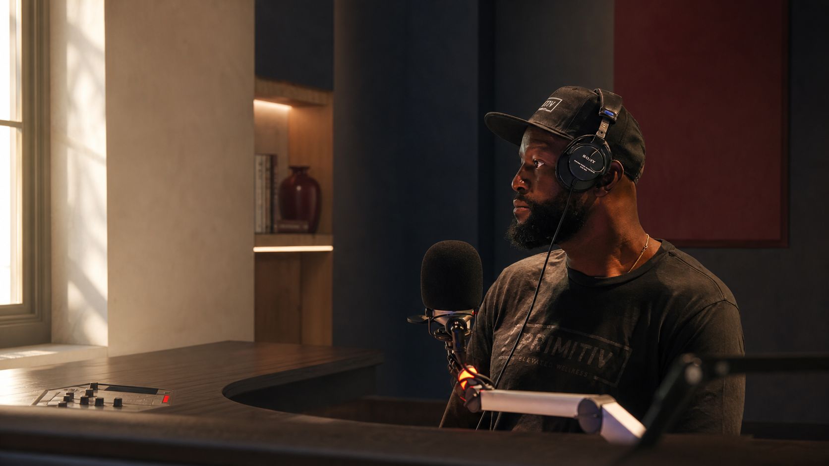 Gosder at a microphone in a quiet studio, looking toward the window
